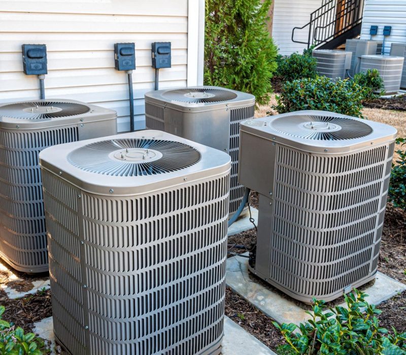 4 HVAC units installed outside of an apartment building. The area is surrounded by greenery